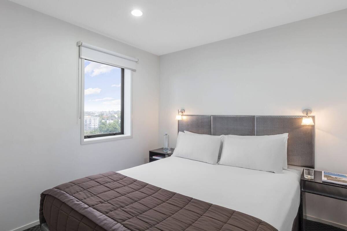 A hotel room with a large bed, a window with a view, and a nightstand with a lamp.
