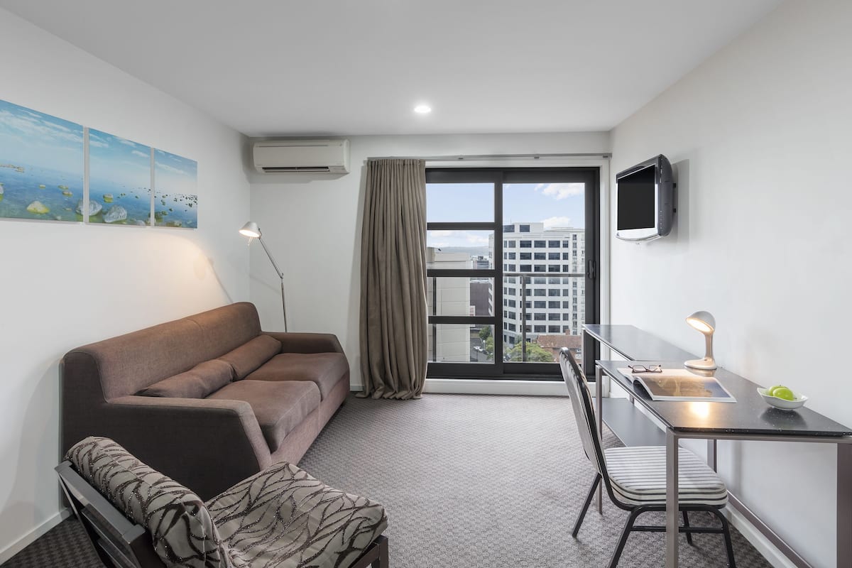 A modern room with a sofa, a dining table, a TV, and a large window with a view of buildings.