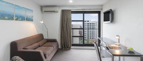 Ein modernes Zimmer mit Sofa, Esstisch, Fernseher und einem großen Fenster mit Blick auf Gebäude.