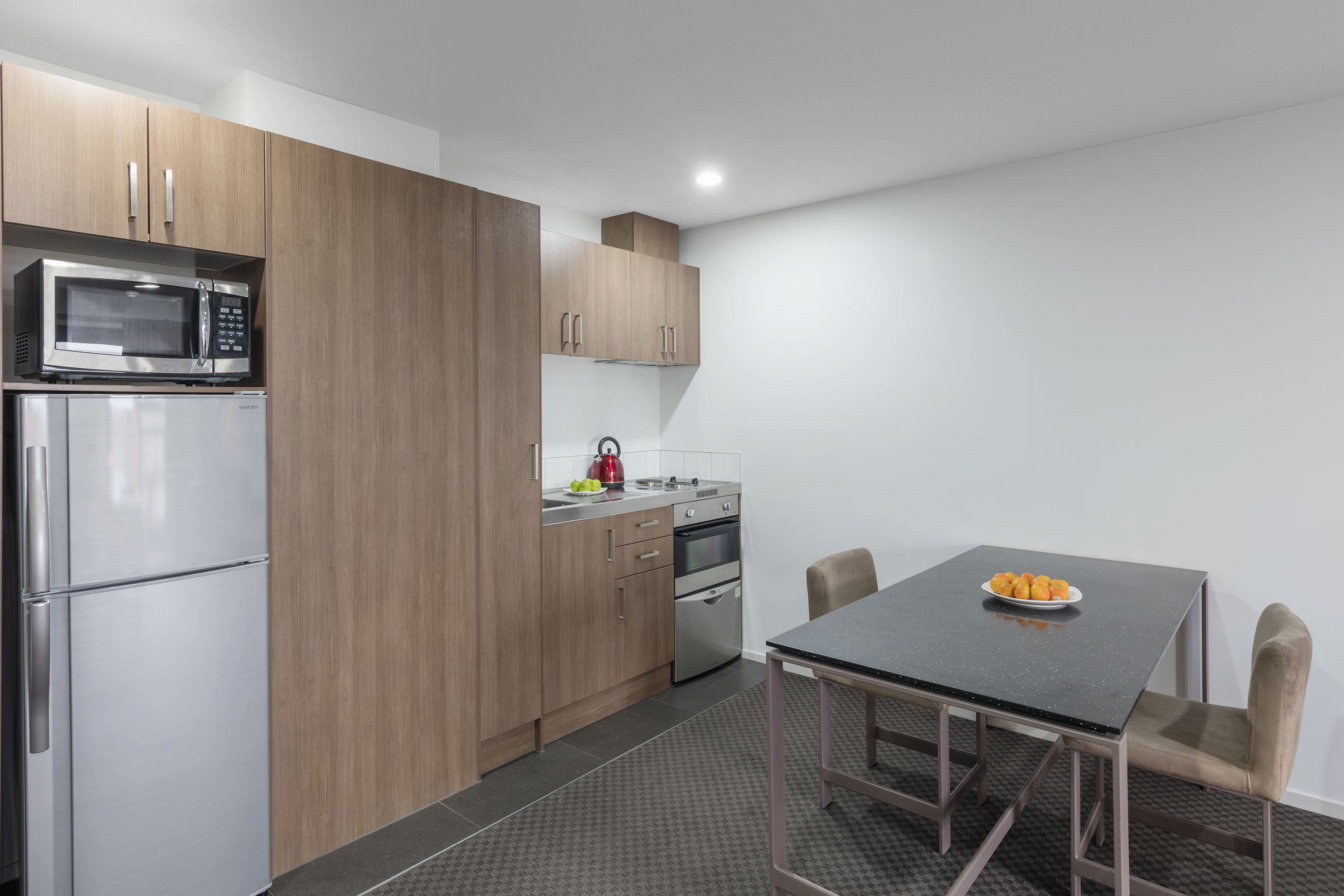 A modern kitchen with stainless steel appliances, wooden cabinets, and a dining area with a table and chairs.