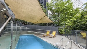 Piscina con barrera de vidrio, dos sillas de descanso amarillas y una gran marquesina.