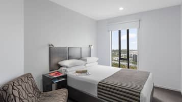 Een hotelkamer met een groot bed, een nachtkastje met een lamp, een stoel en een raam met uitzicht op de stad.