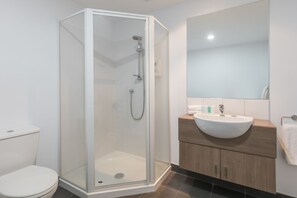 Uma casa de banho moderna com cabine de chuveiro de vidro, lavatório branco e toucador de madeira.