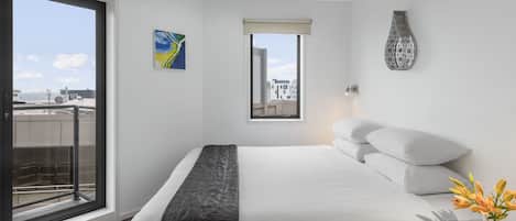 A modern hotel room with a large bed, a view of the city, and a balcony.
