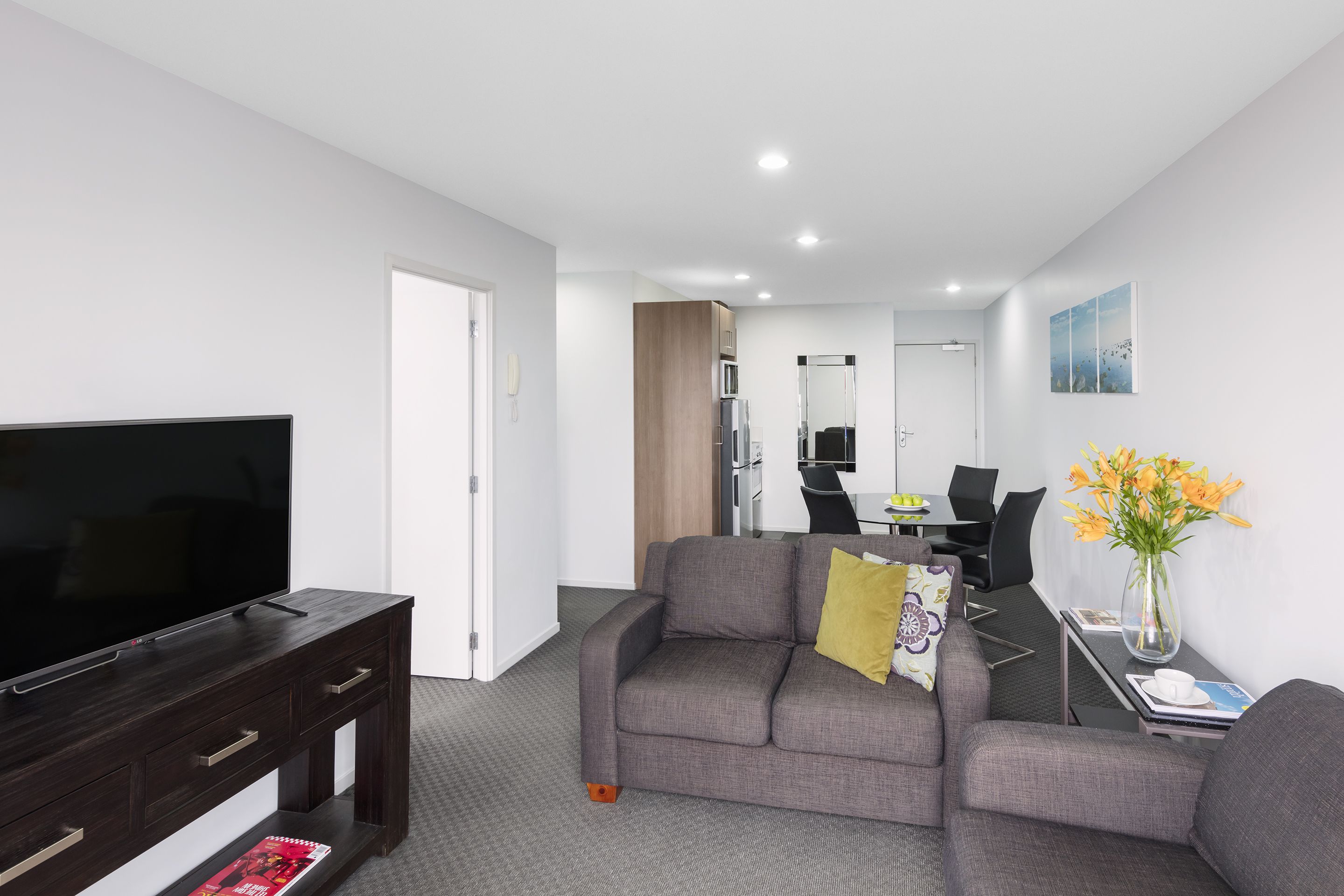 A modern living room with a flat-screen TV, a gray sofa, a coffee table, and a dining area with a table and chairs.