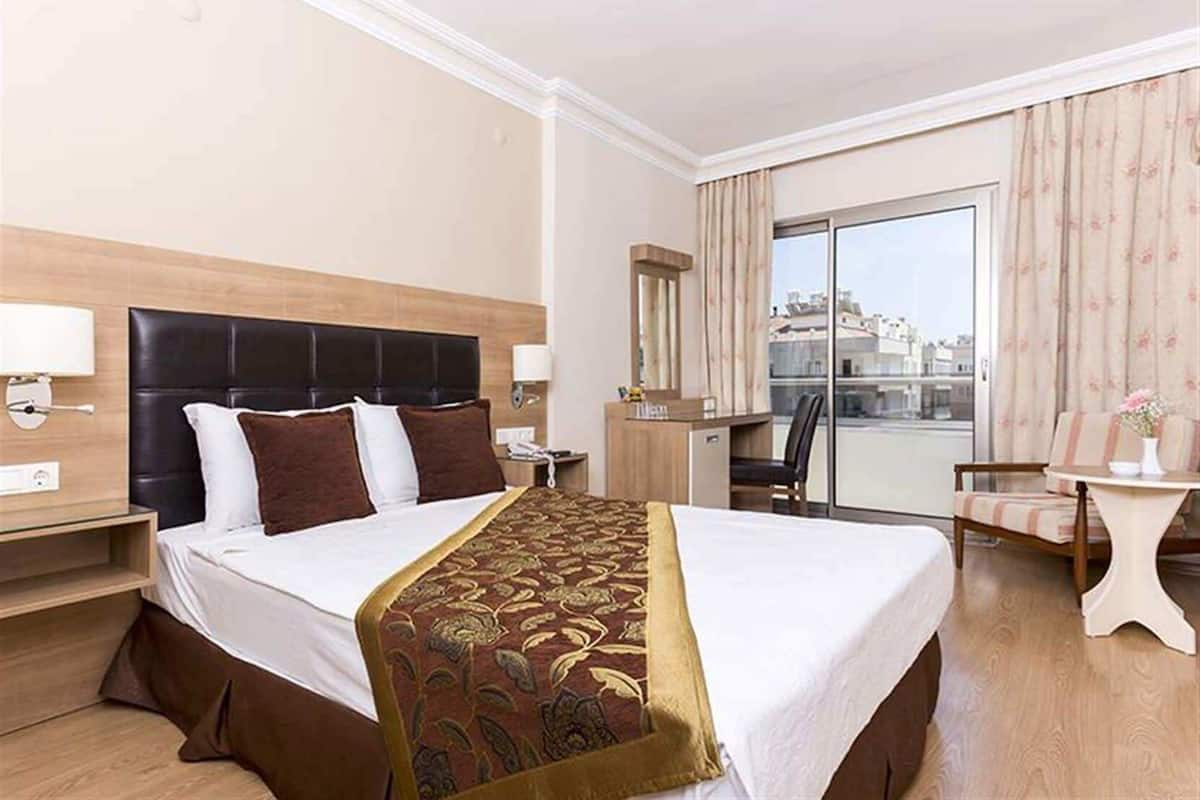 Une chambre d’hôtel avec un grand lit, un bureau, une chaise et une vue sur la ville par la fenêtre.
