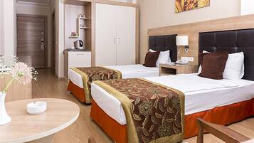 A hotel room with two beds, a desk, a chair, a small table, a vase with flowers, and a painting on the wall.