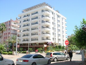 A multi-story hotel with balconies, a stop sign, and a street with cars and pedestrians. - Suite Laguna Hotel (Antalya)