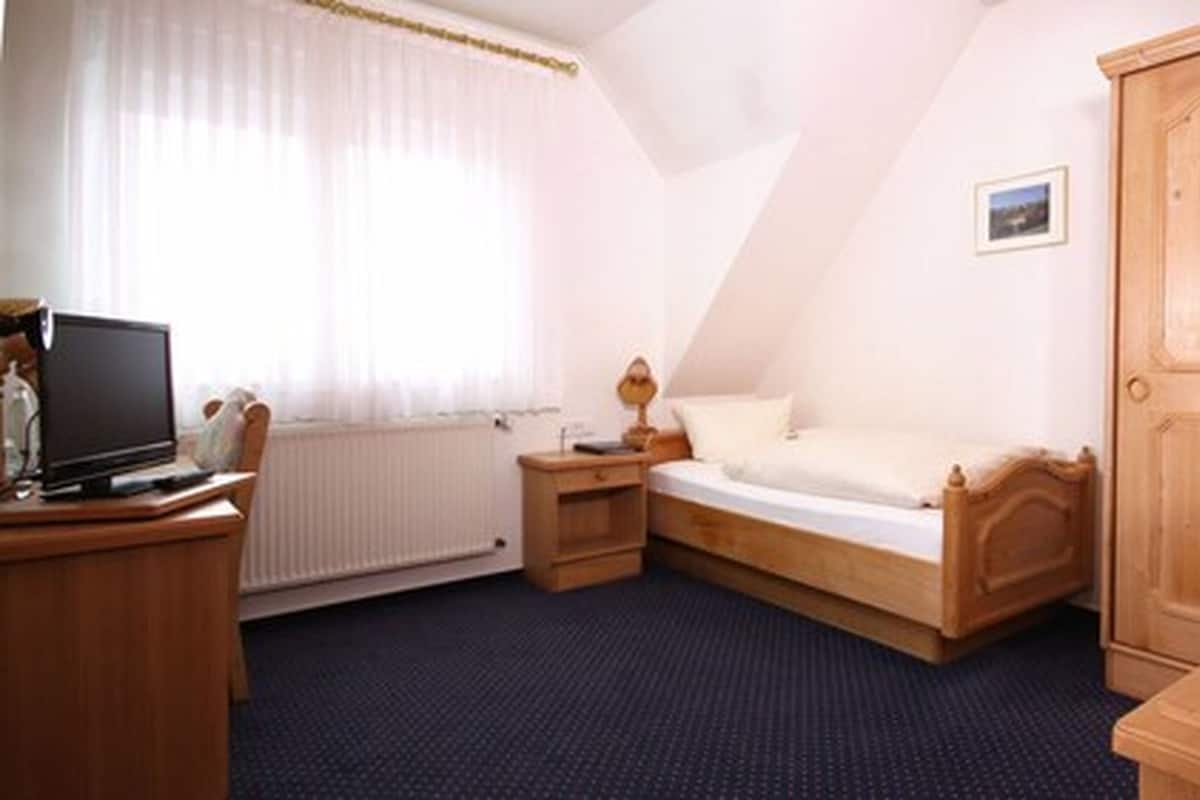 Ein Schlafzimmer mit Bett, Schreibtisch mit Computer, Kleiderschrank und Heizkörper.