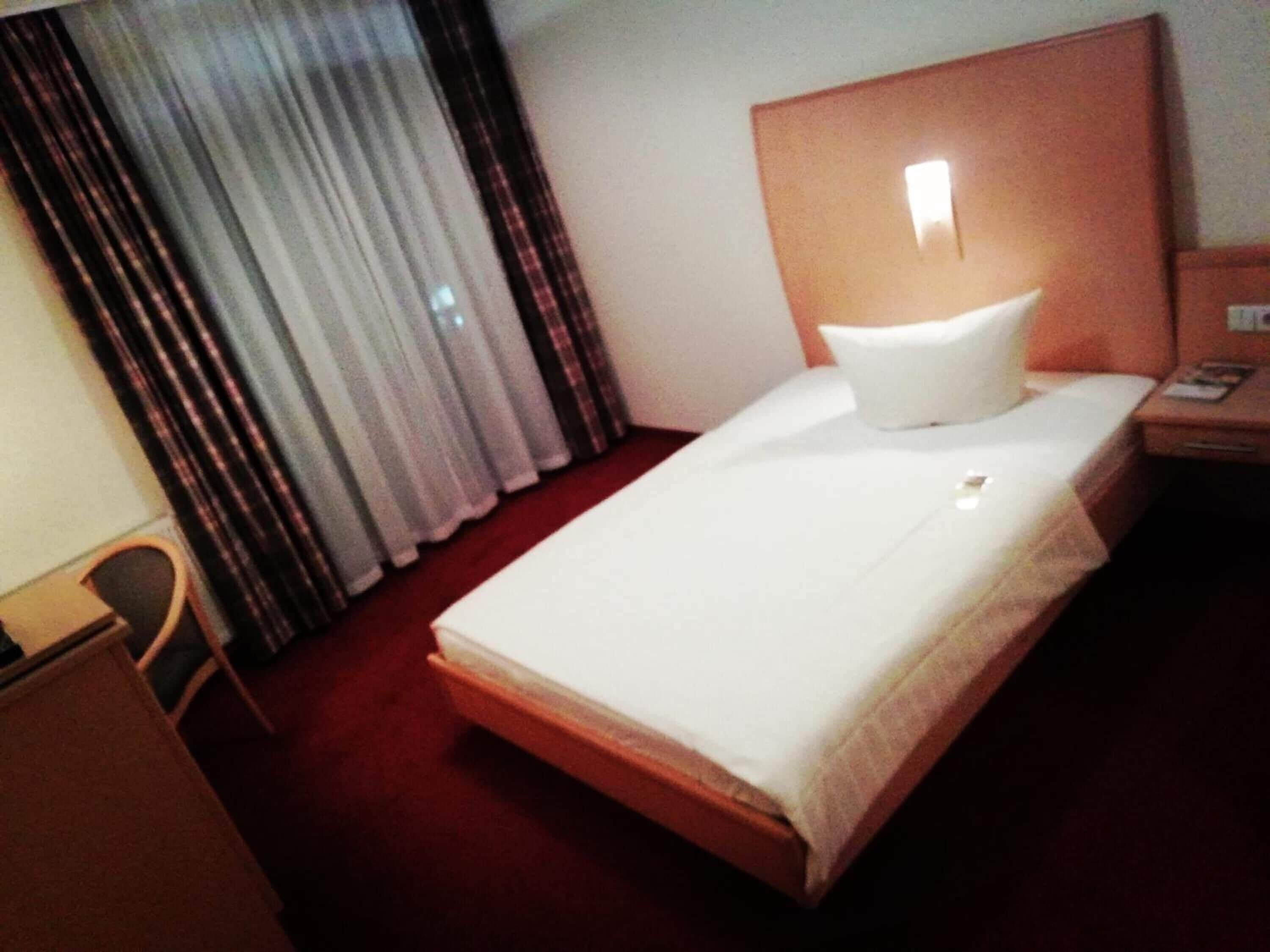 A hotel room with a bed, a nightstand, a chair, and a window with curtains.