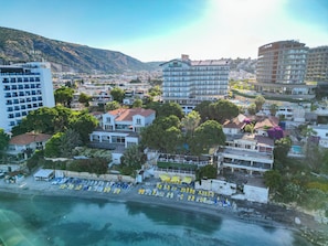 Un pueblo costero con una playa, edificios de hotel y montañas al fondo.