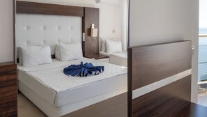 A modern hotel room with a large bed, a wooden headboard, a bedside table, and a view of the sea. - Arora Hotel (Kusadasi)