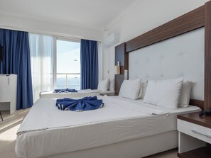 Ein Hotelzimmer mit einem großen Bett, einem Nachttisch, einem Schreibtisch und einem Fenster mit Vorhängen.
