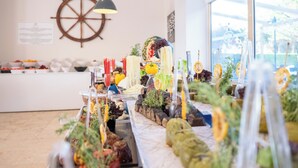 A buffet with various food items, a ship's wheel decoration, and a large window. - Arora Hotel (Kusadasi)