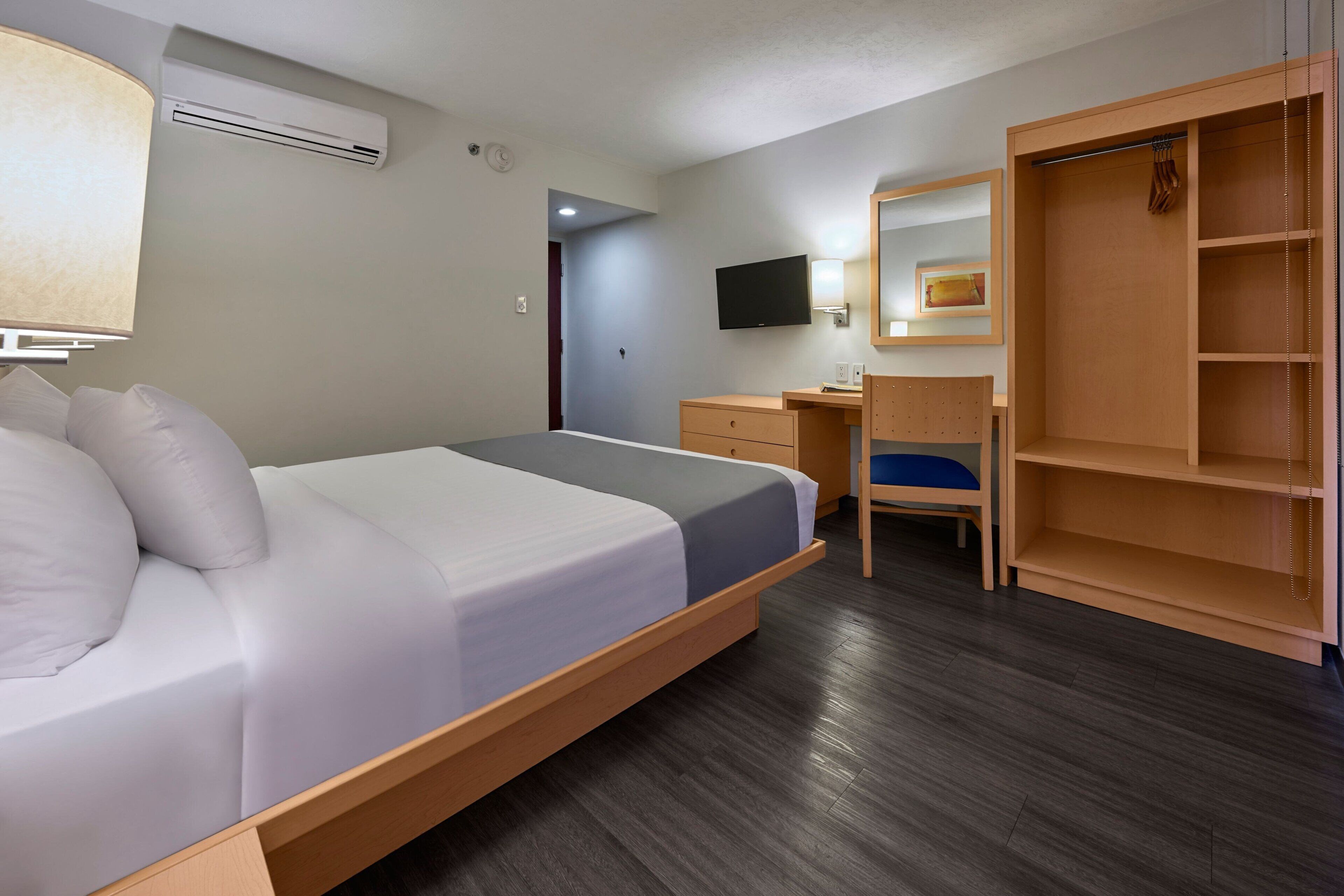 A hotel room with a bed, desk, chair, wardrobe, and a TV mounted on the wall.