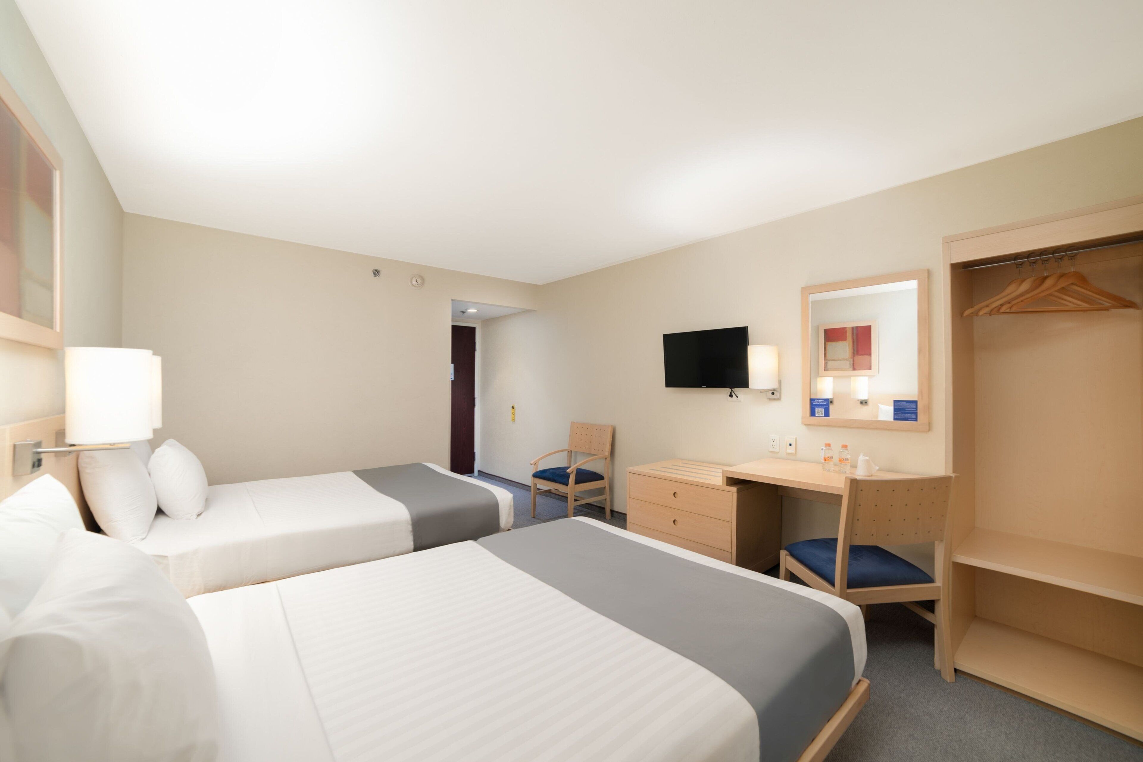 Une chambre d’hôtel avec deux lits, un bureau, une chaise, une armoire et un téléviseur.