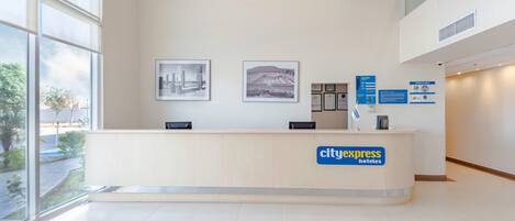 Un mostrador de recepción con vistas a la ciudad, cuadros en la pared y un cartel de CityExpress Hotels.