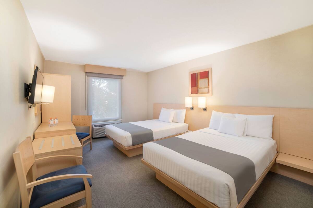 A hotel room with two beds, a desk, a chair, a TV, and a window.