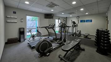 Un gimnasio con máquinas de cardio, pesas libres y una banca.