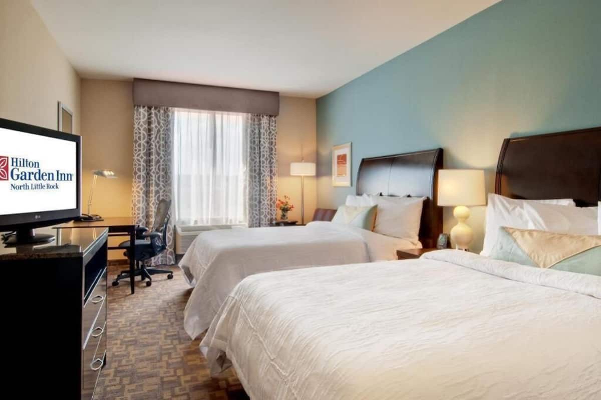 A Hilton Garden Inn North Little Rock room with two beds, a desk, a TV, and a window with curtains.