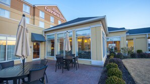 A hotel patio with outdoor seating and a large windowed area. - Hilton Garden Inn North Little Rock (North Little Rock)