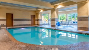 An indoor swimming pool with clear blue water, a tiled deck area with chairs, and a door leading to another room. - Hilton Garden Inn North Little Rock (North Little Rock)