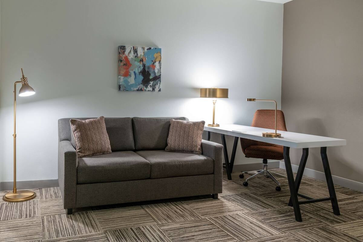 A modern living room with a grey sofa, two lamps, a white table, and a colorful abstract painting on the wall.