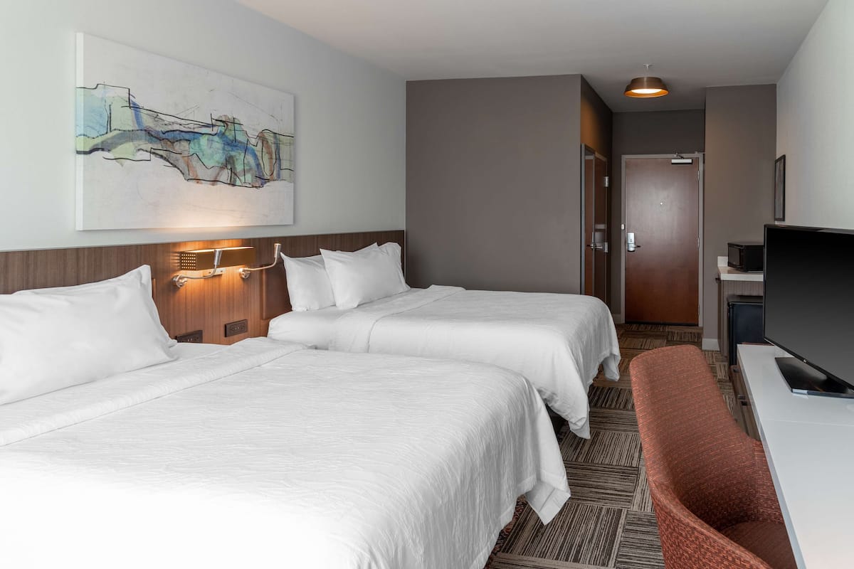 A hotel room with two beds, a television, and a painting on the wall.