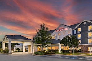 A Hilton Garden Inn with a covered entrance, a parking lot, and a clear sky.