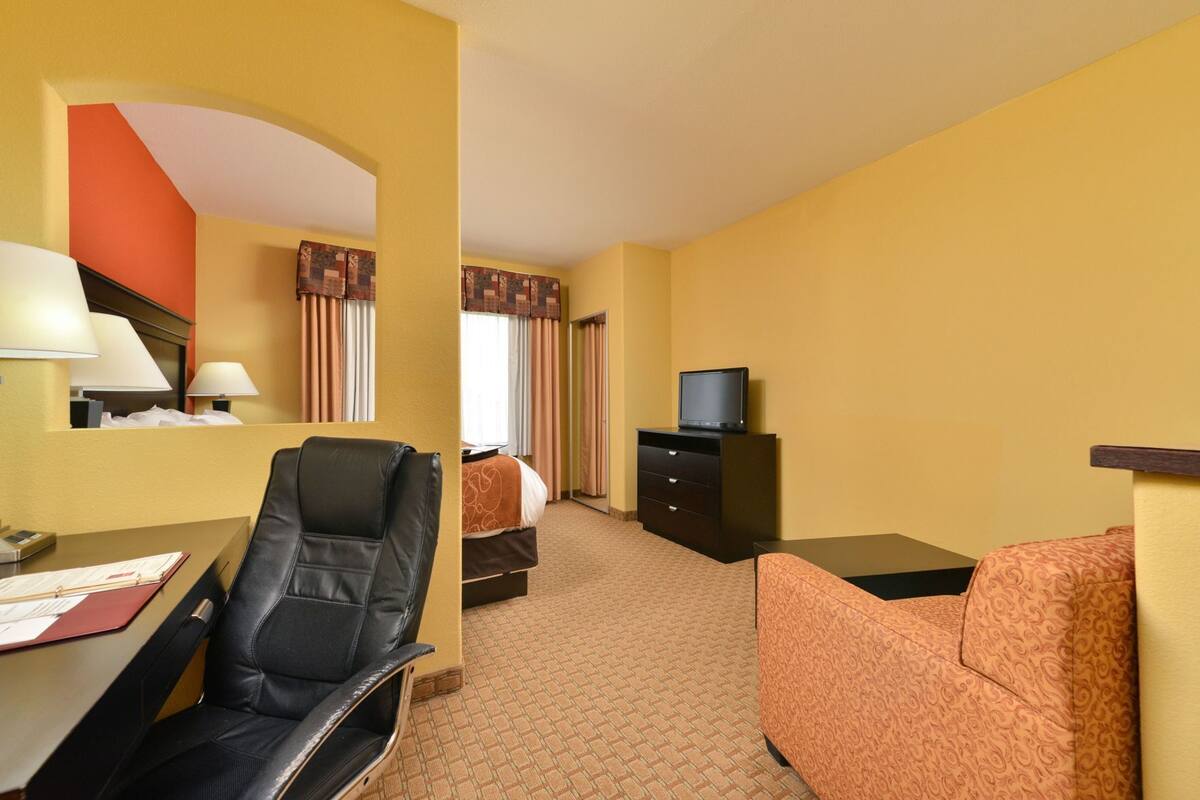 Een hotelkamer met een bureau, een stoel, een bed, een televisie op een dressoir en een gestreept bankje.