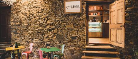 Un café acogedor con pared de piedra, escalera de madera y un letrero que dice 'Caffè Milanò'.