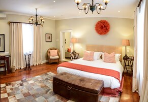 A bedroom with a large bed, a chandelier, a round wall decoration, and a wooden bench.