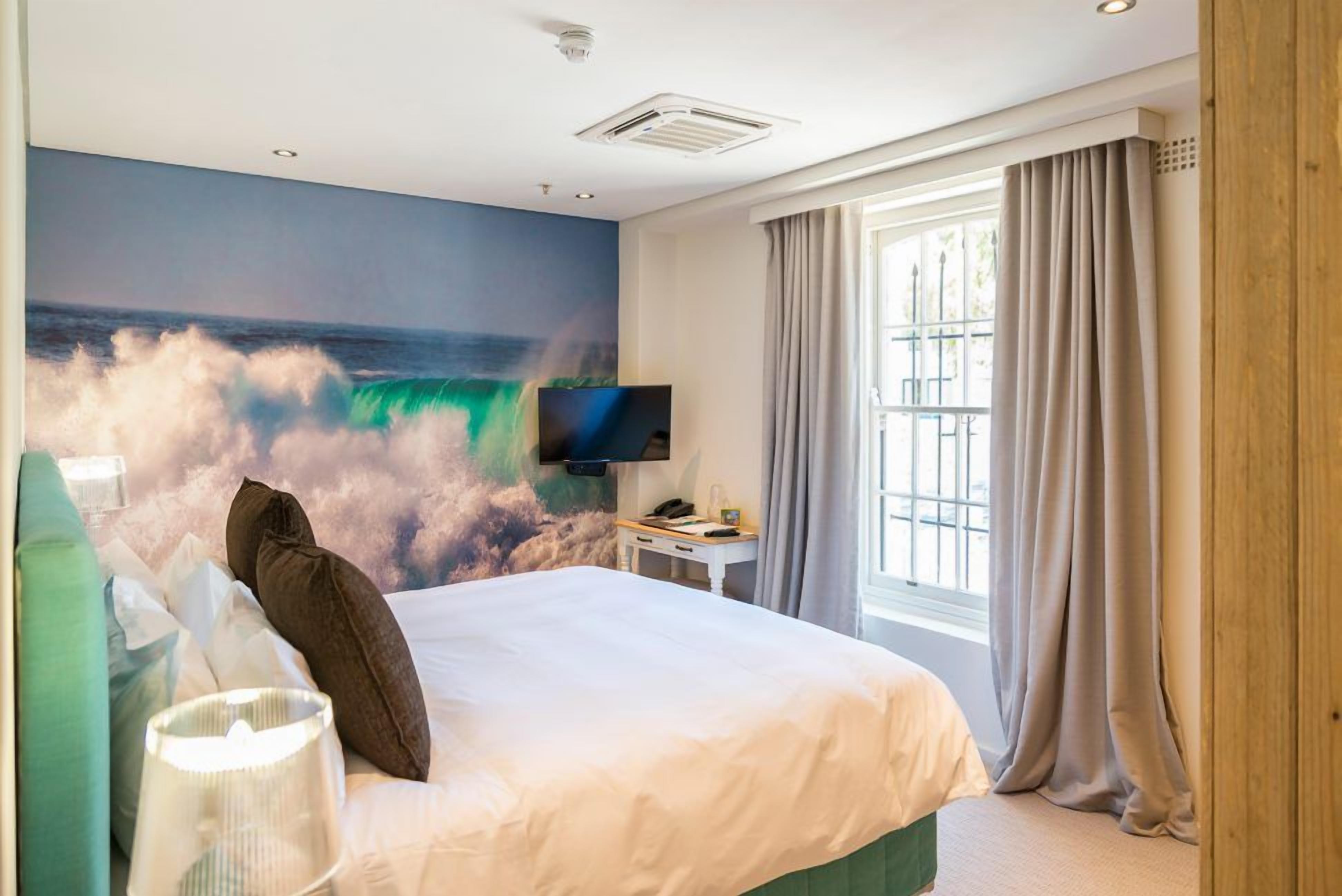 Ein Hotelzimmer mit einem Bett, einem Flachbildfernseher, einem Fenster mit Vorhängen und einem Wandbild einer Welle.
