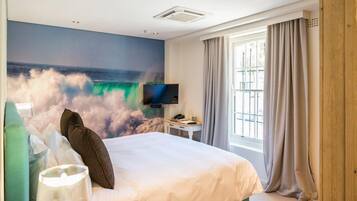 Ein Hotelzimmer mit einem Bett, einem Flachbildfernseher, einem Fenster mit Vorhängen und einem Wandbild einer Welle.