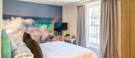 Ein Hotelzimmer mit einem Bett, einem Flachbildfernseher, einem Fenster mit Vorhängen und einem Wandbild einer Welle.