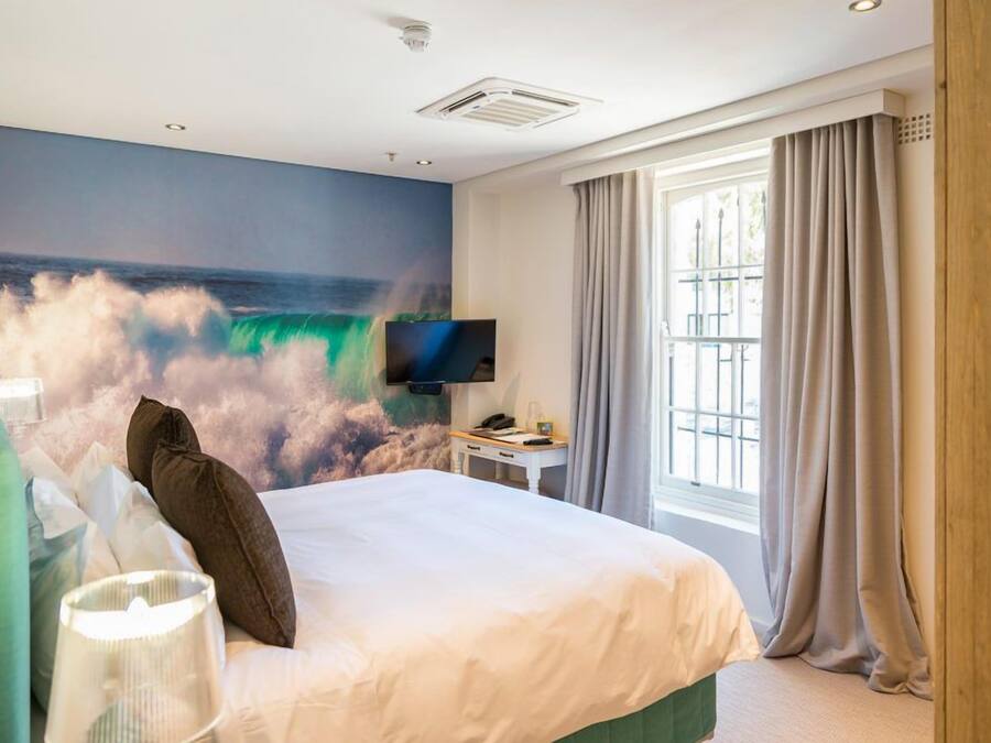 Ein Hotelzimmer mit einem Bett, einem Flachbildfernseher, einem Fenster mit Vorhängen und einem Wandbild einer Welle.