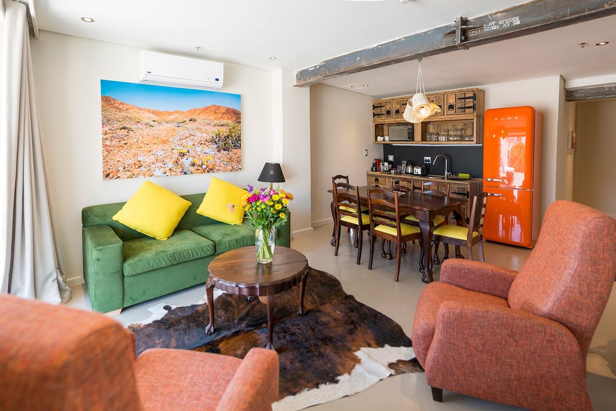 A living room with a green sofa, orange armchair, dining table, and a mounted air conditioner.