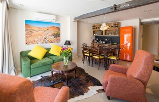 A living room with a green sofa, orange armchair, dining table, and a mounted air conditioner.
