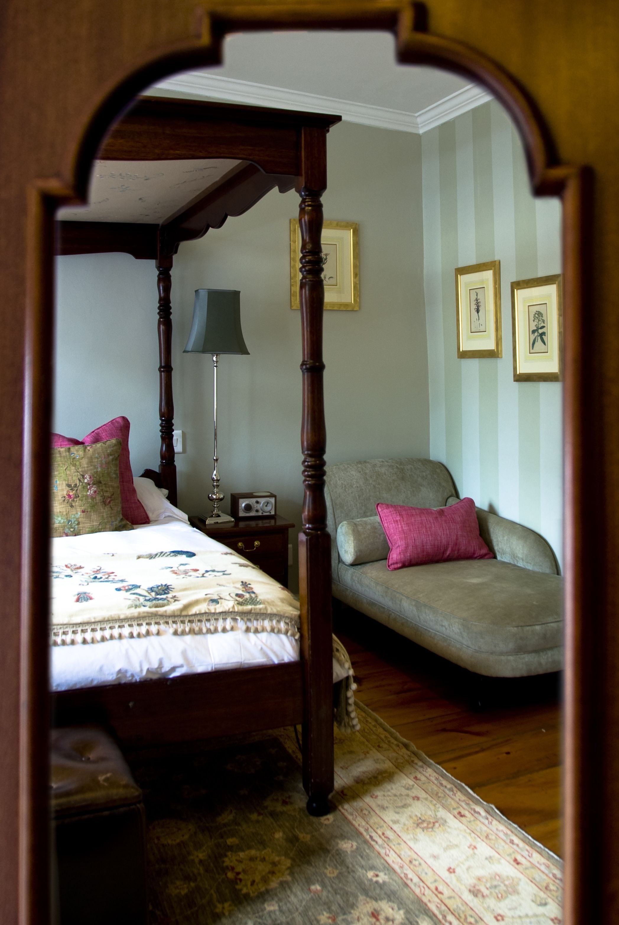 Un dormitorio con cama con dosel, una mesita de noche, una silla y una lámpara.