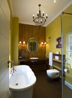 A bathroom with a freestanding bathtub, a round mirror, a toilet, and a shower area.