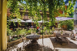 An outdoor patio area with tables and chairs, surrounded by potted plants and umbrellas.