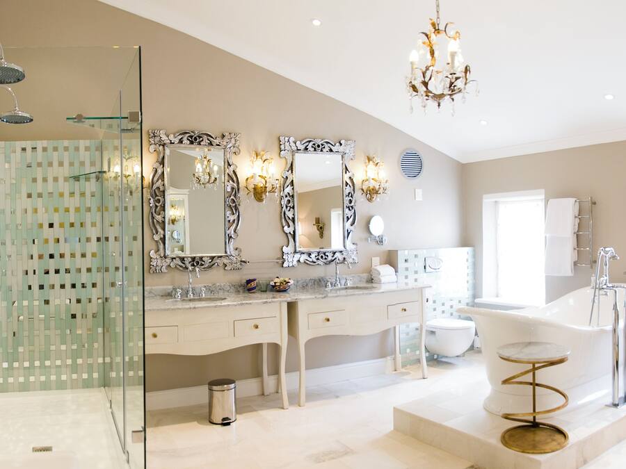 A spacious bathroom with a glass shower enclosure, a double vanity with ornate mirrors, a freestanding bathtub, and a marble floor.