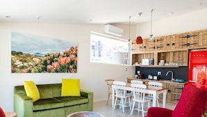 A modern living room with a green sofa, red chairs, a dining table, and a kitchen area with wooden cabinets and a red refrigerator. - Cape Heritage Hotel (Cape Town)