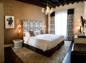 Ein Schlafzimmer mit einem großen Bett, einer Chandelier, einem Nachttisch mit Lampe und einem an der Wand montierten Fernseher.