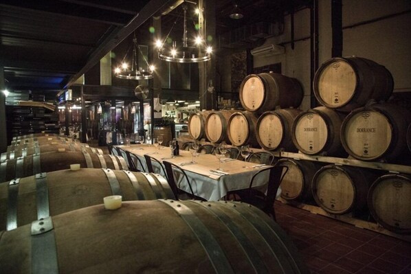 A wine cellar with rows of wooden barrels and tables set up for tasting. - Cape Heritage Hotel (Cape Town)