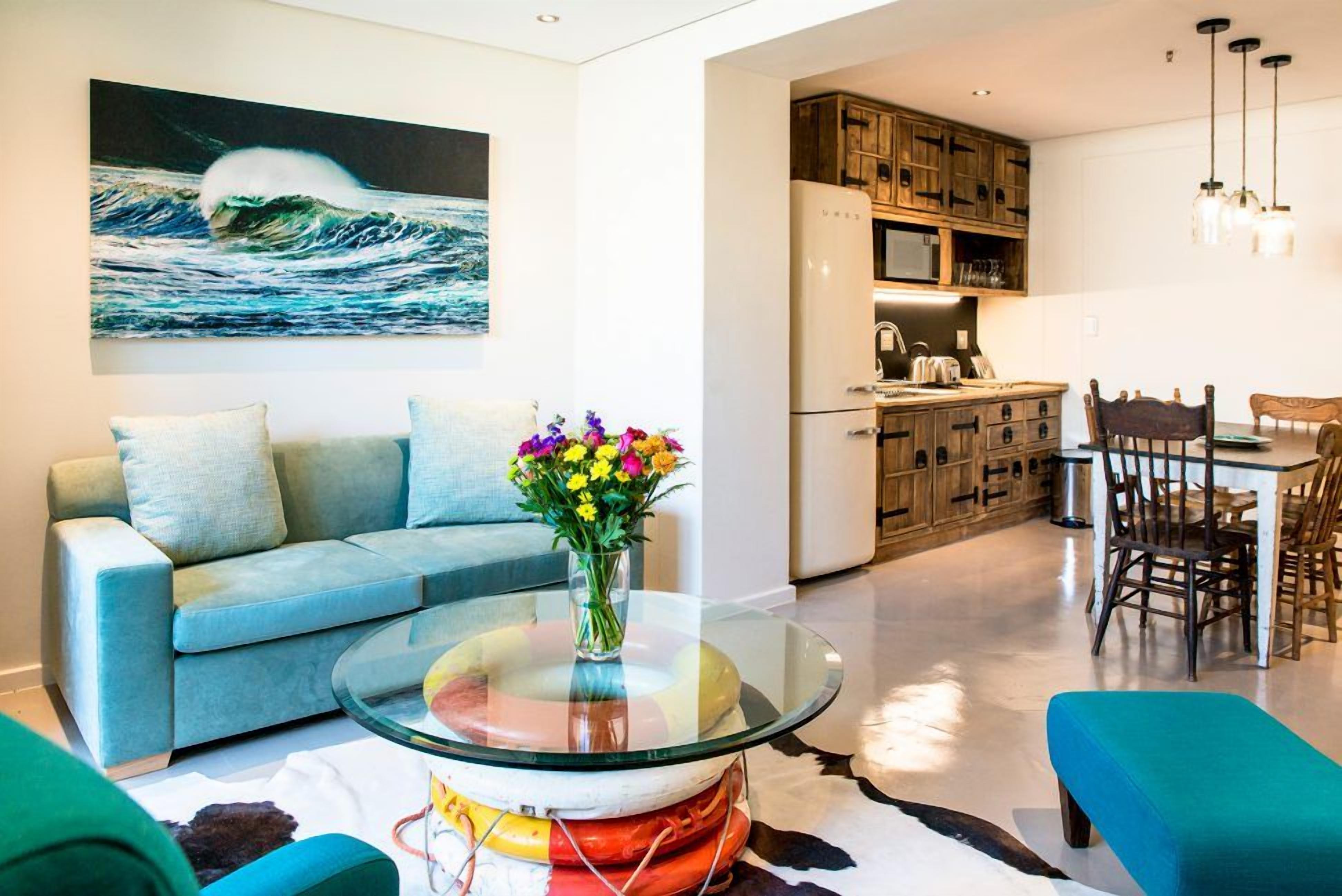 A modern living room with a sofa, a glass coffee table, and a painting of a wave.