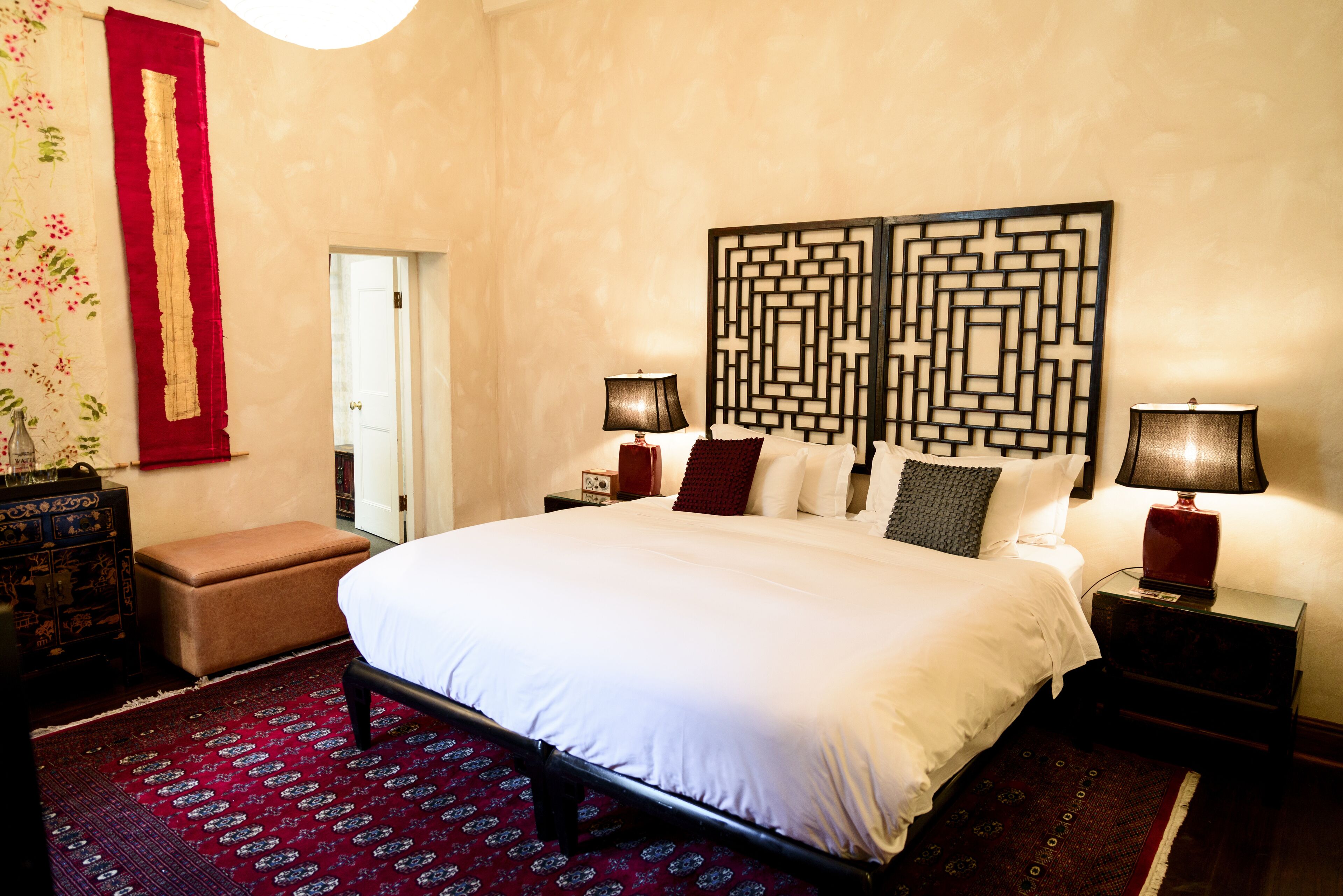 A neatly arranged bedroom with a large bed, two bedside tables with lamps, a red decorative panel, and a patterned rug.