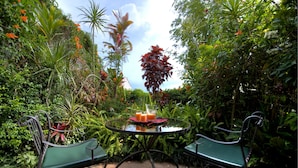 A glass table with two green chairs, surrounded by lush tropical plants and a bench. - Hotel Le Bergerac (San José)