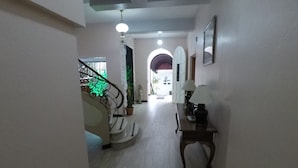 A hallway with a staircase, a table with a lamp, and a framed picture on the wall. - Hotel Le Bergerac (San José)