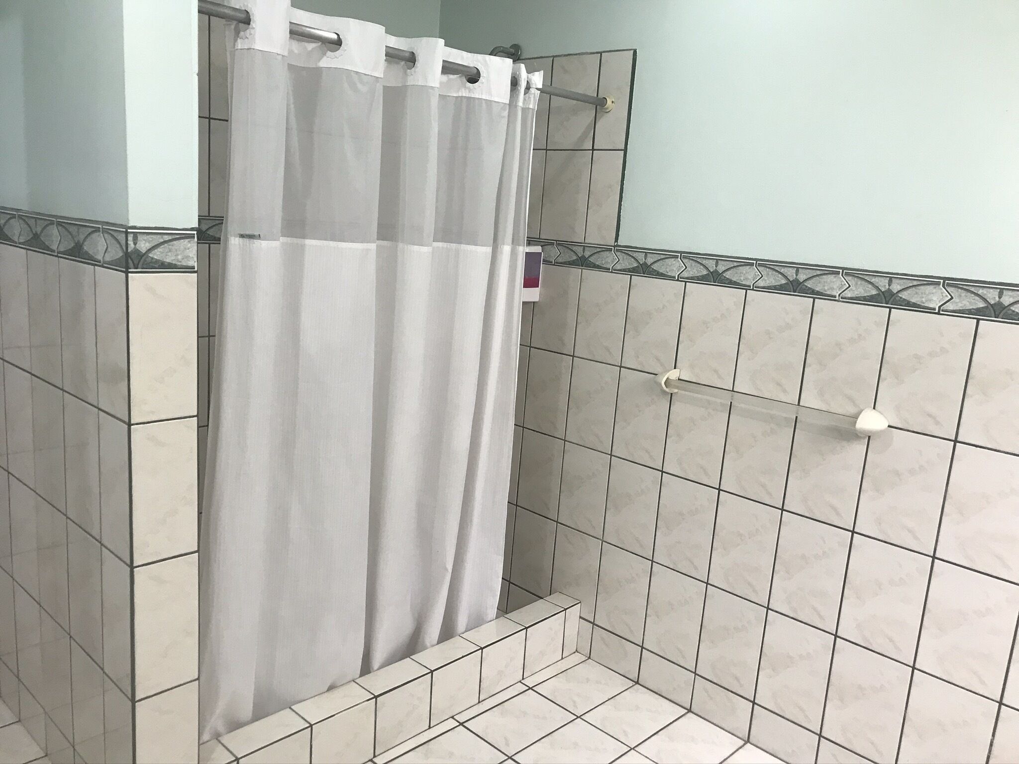 A bathroom with a shower curtain, tiled walls, and a shower control handle.